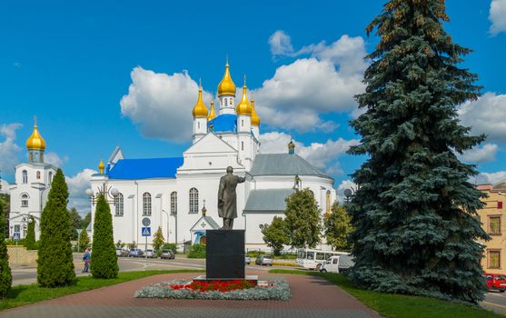 a monument on the city square decorated with a flower bed on the background of the church and a tall spruce rising next to it