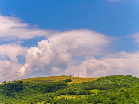 An antenna on the top of a grassy mountain with blurred clouds in the sky