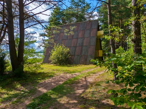 A road in the forest leading to a little house for tourists under a slate roof standing on the shore of a large beautiful lake.