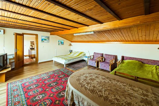A room with a wood ceiling and a carpet on the floor is simply furnished