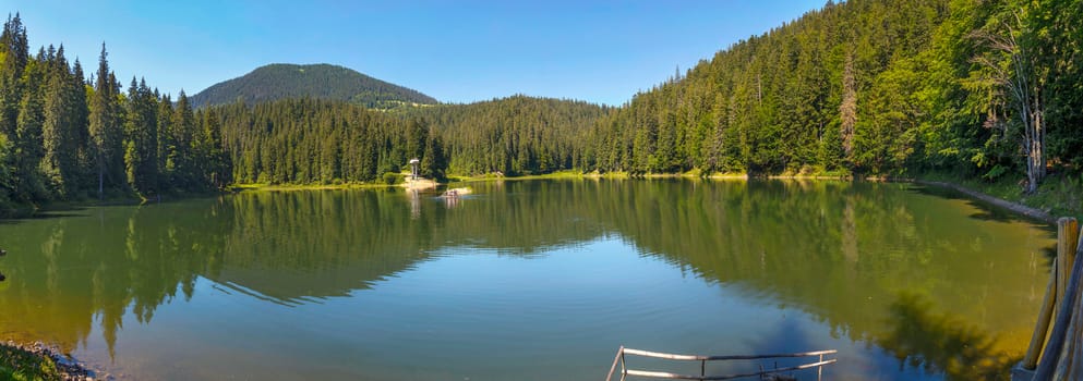 green lake in the mountains among the coniferous forest under the blue cloudless sky. holiday destination, picnic, tourism