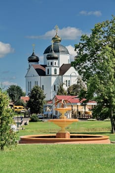 Park area with a fountain in the background of a beautiful temple with white walls, black domes and gold crosses