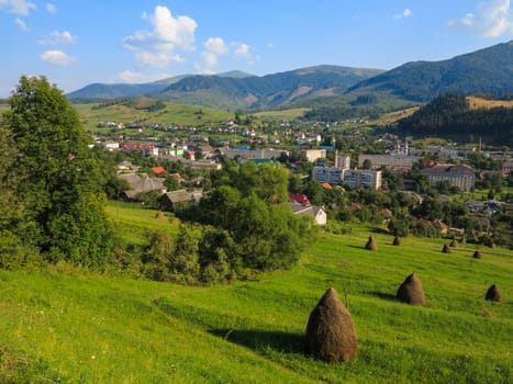 A small town located in a picturesque mountainous area with dry haystacks on the slopes on the outskirts.