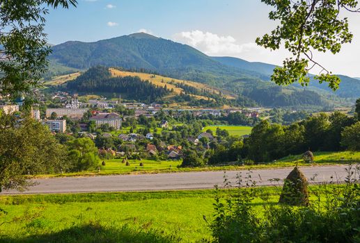 a modern city at the foot of a mountain covered with dense forest, green grass, blue sky. masto for recreation, picnics and tourism