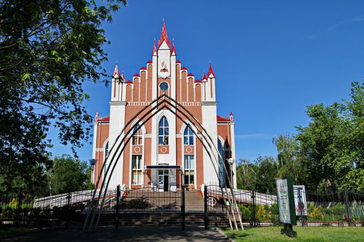 Metal arch in front of the gate leading to the religious house. It is in a beautiful place among the trees against the blue sky.