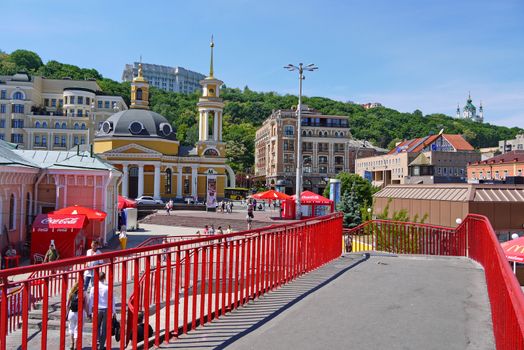 Pedestrian bridge with a red fence on the background of the entrance to the metro and the beautiful yellow church.