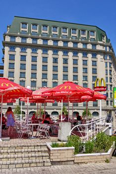 McDonalds Cafe on the terrace with umbrellas on the background of a tall house in the city