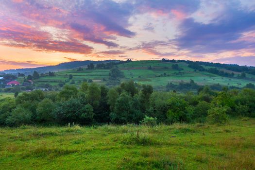 Green mountain slope with houses on it against the background of a dawn or sunset sky. place for rest and travel