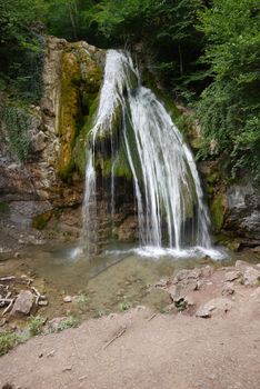 A large beautiful waterfall against the background of a rocky mountain and green plantations