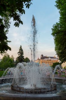 The high spray of a fountain flying over the background of a blue sky in the city park spill over