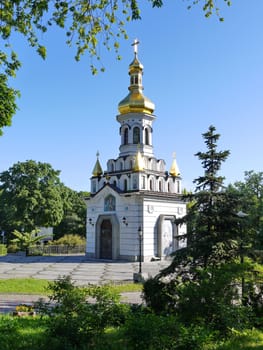 A small, white church with a golden dome on the background of trees