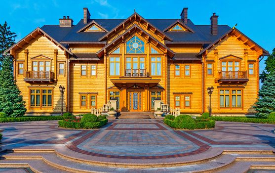 The area is laid out with beautiful patterns from the tile with a green lawn growing on it in front of the house with sheathed wood and windows of different shapes.