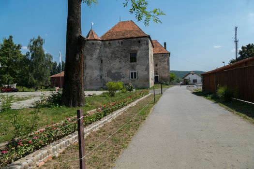 An old, gray building with a tiled red roof and a road around it