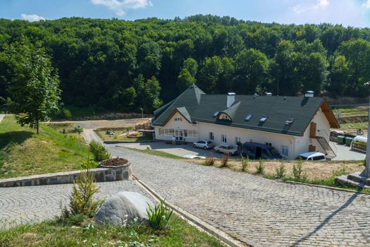 The access road from the cobblestones leads to a large house, a hotel drowning in green trees against the blue sky