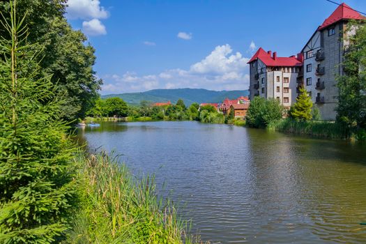 A small river in the background of mountains with green thickets on one and the shore and high-rise buildings on the opposite.