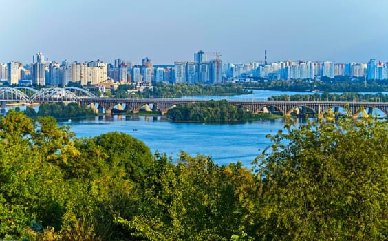 A magnificent landscape with a bridge going through a wide river against the backdrop of city skyscrapers.
