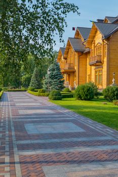 The path in the park is laid out of tiles in the form of squares leading to a luxurious house made of wood.