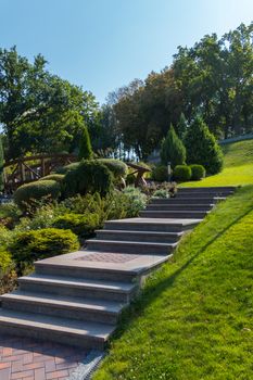 The steps in the park are laid out of the tiles going up the hillock with a green lawn on one side and figured shrubs on the other.