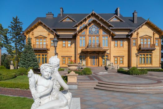 white statue of an angel on a terrace near a large wooden house in a park with alleys