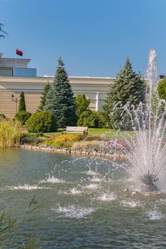 A bench for relaxation near the pond with a beautiful view of the fountain in the water and the beautiful nature around.