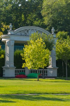 white arches with columns in the park against the backdrop of lush green trees near which lies buoy