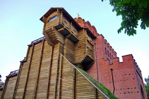 A tall ancient temple of red brick in one half and a wooden building on the other side.