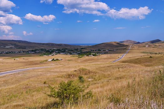 a long empty road, passing through a dry valley covered with grass among the mountains against a blue cloudy sky. place of rest, tourism, picnic