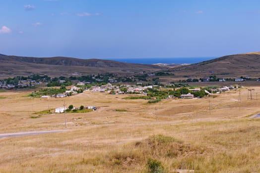 the town spread out in a valley covered with dry yellow grass, on which the road runs along the background of the hills