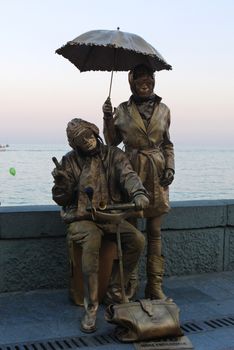Brass monument to a man and a woman with an umbrella, in tank helmets and glasses