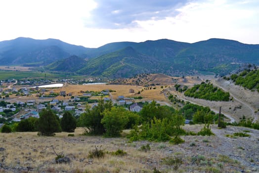 A neat village lying in a picturesque valley with rare trees growing on the slopes and cobwebs of dirt roads around.