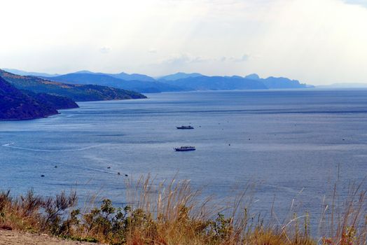 A wide blue sea with pleasure ships and boats against the background of high boundless mountains