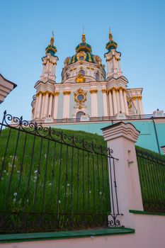 A tall temple with golden domes surrounded by a fence made of wrought iron