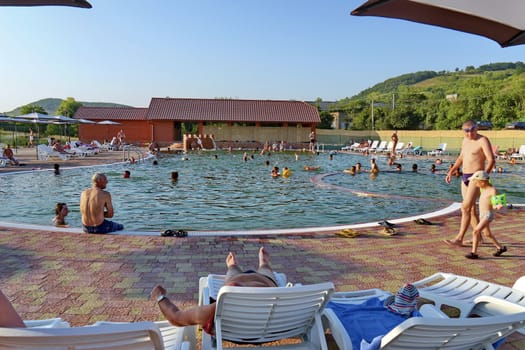 joyful people having a rest on sunbeds and swimming in a pool on a background of nature
