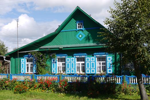 blue or turquoise wooden house with shutters with a painted fence, flowers and trees against a blue cloudy sky. place of rest and tourism