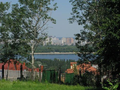 A panorama of urban multistory buildings in a green park on the river bank