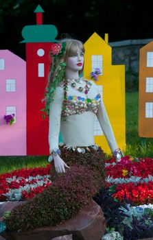 Mermaid of flowers in a flowerbed with beautiful flowers in the background of the decorated toy city.