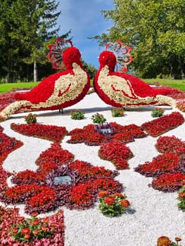 The composition in the park on the green slope is entirely composed of flowers planted with beautiful ornaments and standing opposite each other as if admiring birds.