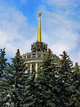 An ancient architectural work with a golden star and columns in the shadow of fir branches. This is a landmark of the city.