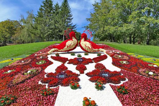 arabesque flower bed with a large number of white and red shades of flowers in the form of two birds on the hill