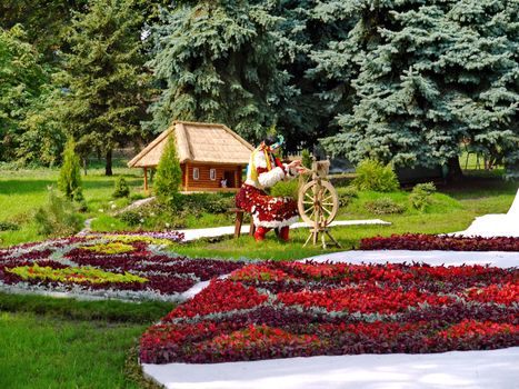 Girl-weaver in national Ukrainian clothes near flowerbeds with flowers on the background of the Ukrainian village house.