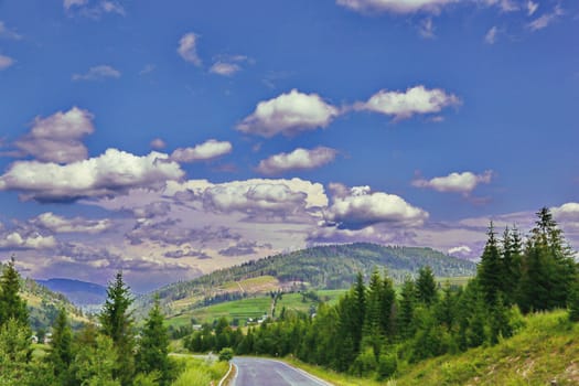 fantastic clouds in the blue sky above the road between the green mountains of Carpathians
