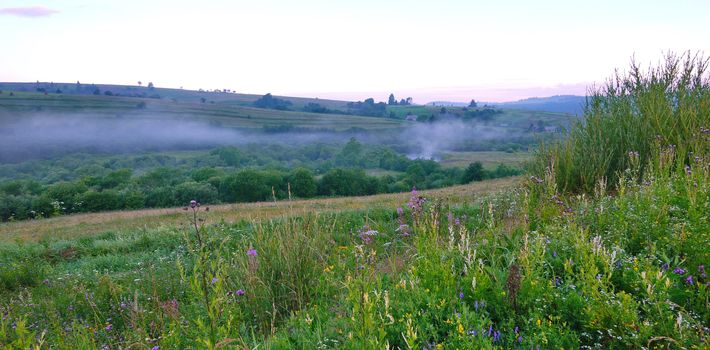 The beam between the green hills is covered with smoke. Probably someone cooks porridge at the stake