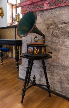 An ancient painted gramophone near a stone wall next to rare furniture and a samovar on a windowsill