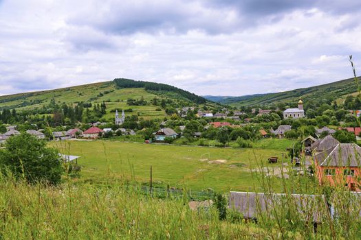 A small rural village with many houses and several churches at the foot of the gentle green mountain
