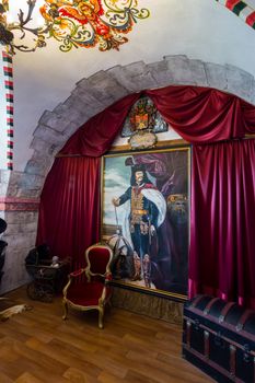 A beautiful painting in the museum with an antique chair standing by a rustic red cloth and a chest of wood closing on the latches.