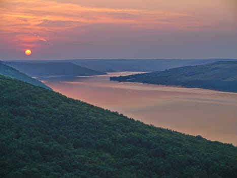 A picturesque view of the river bay in the middle of the green mountains against the evening sunset