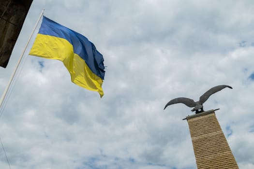A yellow-blue flag and a bird on the monument against a white background from the clouds of the sky