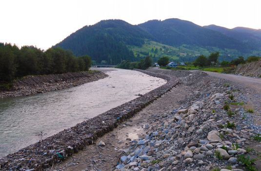 A swift mountain river with stone banks on both sides against the background of a high green mountain