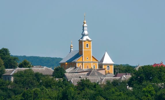 Against the background of the blue sky, the church tower with a dome of gold casting in the sun with slate roofs of houses next to it.