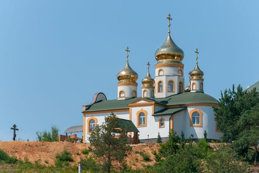 A beautiful white temple with golden domes on a green hill shines with the sun's rays